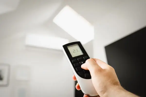 手持冷氣遙控器調整室內溫度，象徵冷氣選購與省電判斷