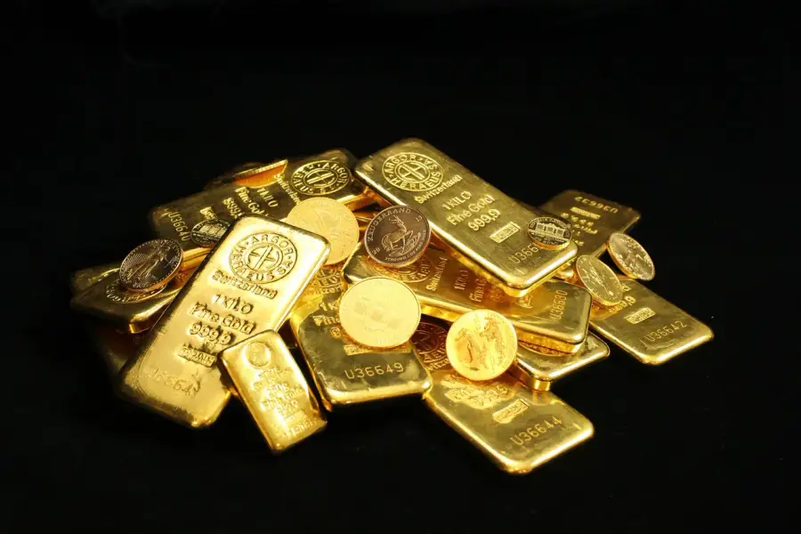 金價走勢圖與黃金實體在分析師桌面上並置，畫面中可見一段上揚與一段下滑的趨勢線