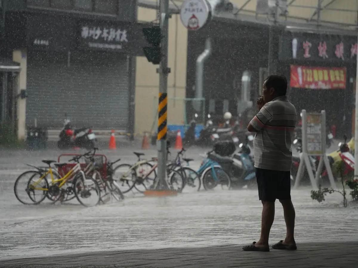 豪雨中的台灣街道與騎樓，一名行人站在積水路面旁，呈現天然災害期間的停班停課情境（示意圖）