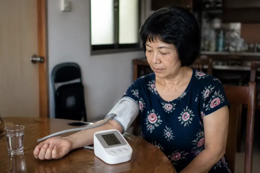 民眾在家坐著、上臂綁著臂式電子血壓計、袖帶與心臟同高進行居家血壓量測