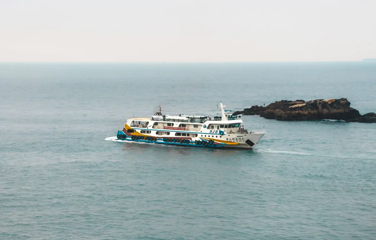 一艘白色客運渡輪航行在海面上，遠方可見島嶼礁岩