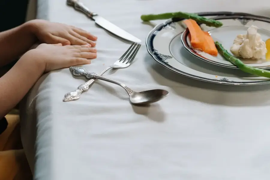 幼兒手部靠近放有蔬菜與熟悉食物的餐盤，呈現家庭餐桌上的挑食情境