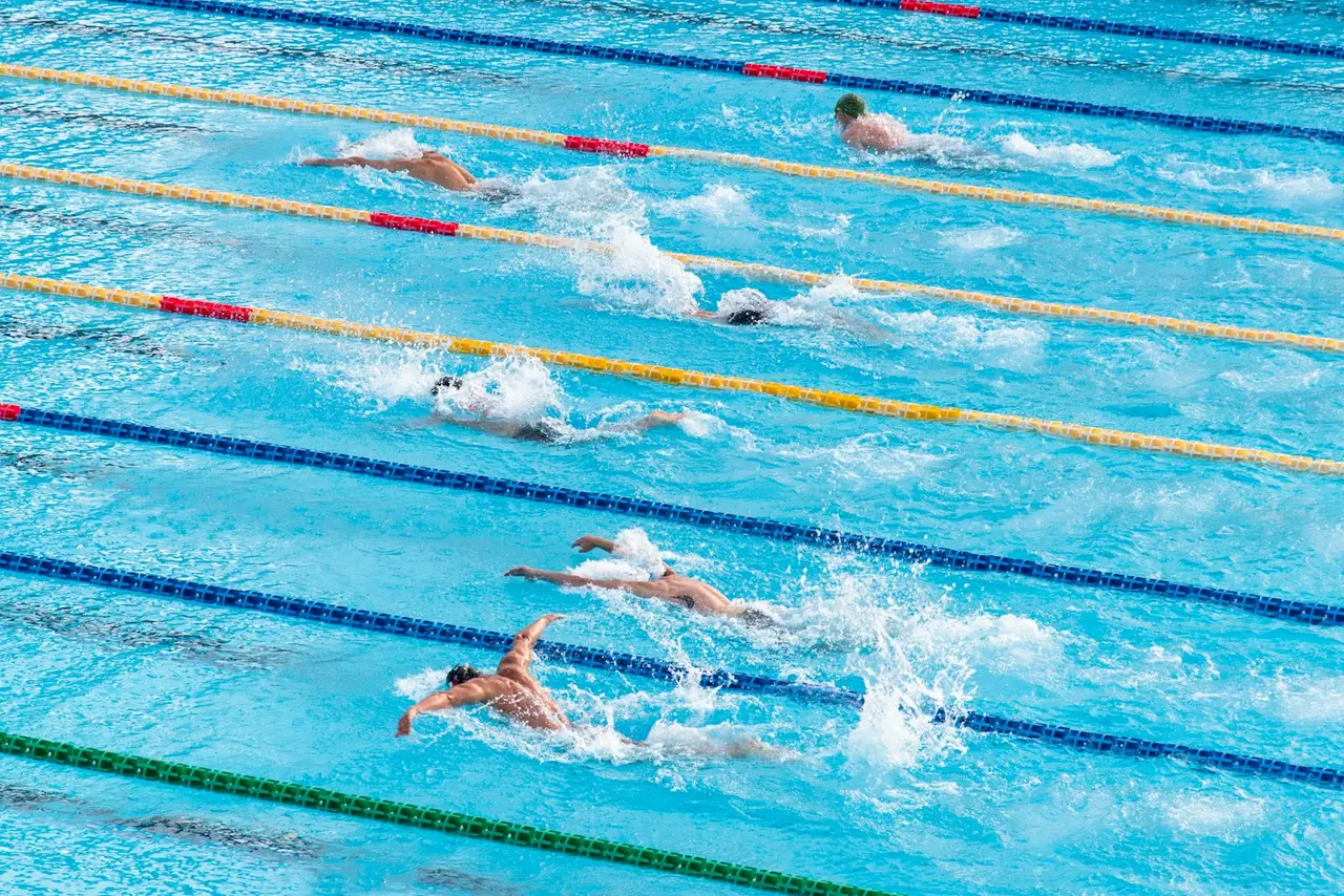 一名男性蝶式選手在室內奧運規格泳池中奮力划水衝刺，激起陣陣水花的動作畫面