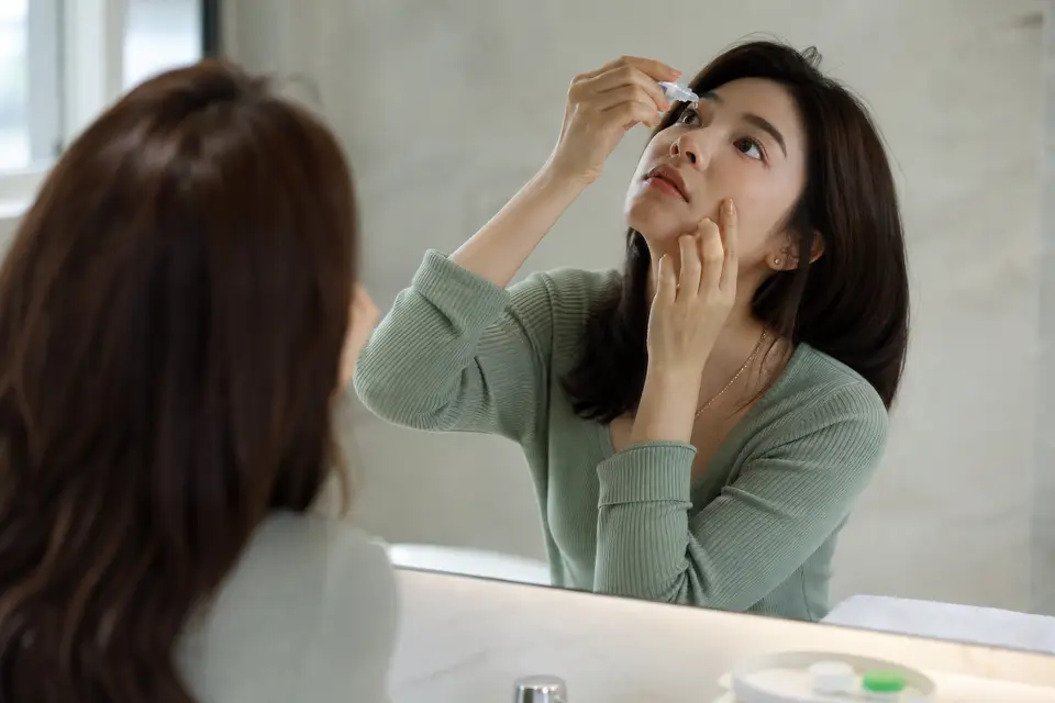 一個人對著鏡子點人工淚液，準備取下隱形眼鏡