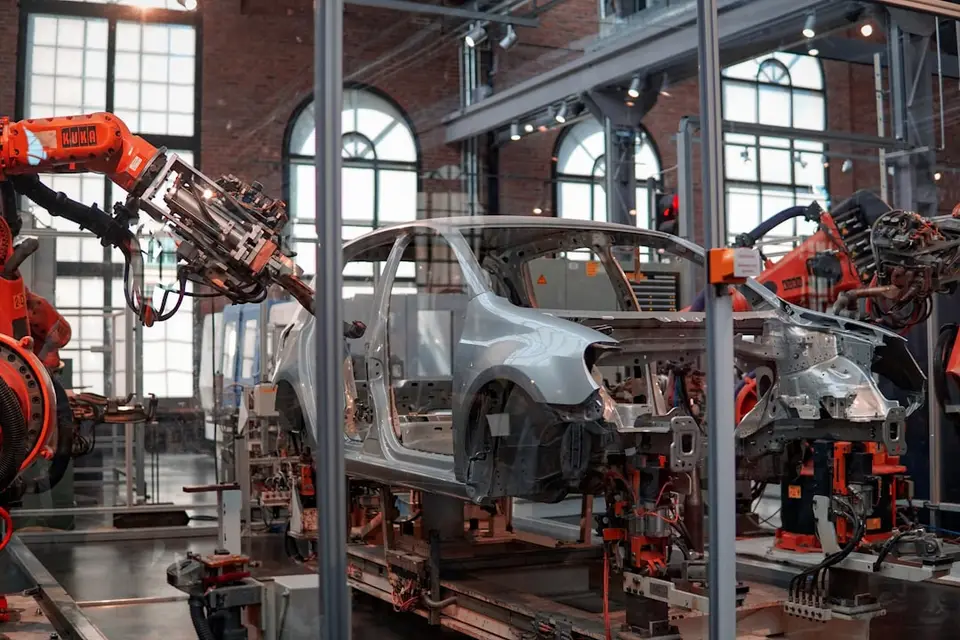 工廠裡的橘色機器手臂在汽車產線上作業，象徵自動化從固定設備走向人形機器人