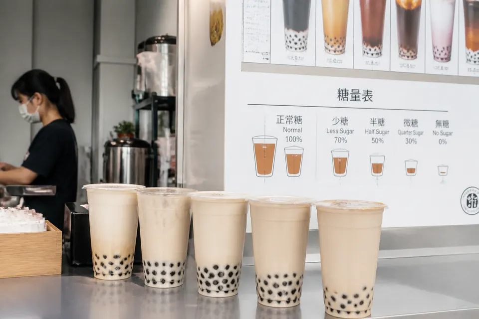 手搖飲料店櫃檯排列著封膜的珍珠奶茶與菜單上的含糖量標示牌