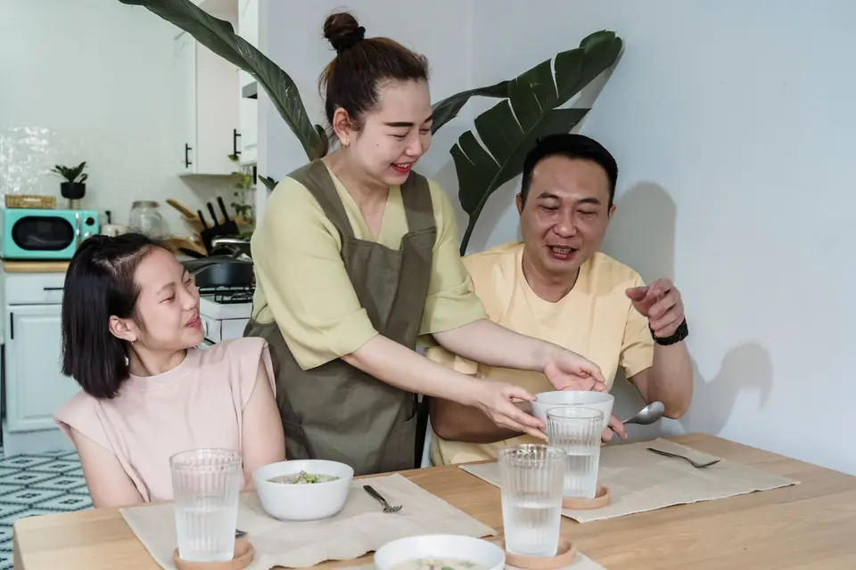 家庭餐桌旁的大人準備食物，呈現陪伴孩子用餐與家長示範的情境