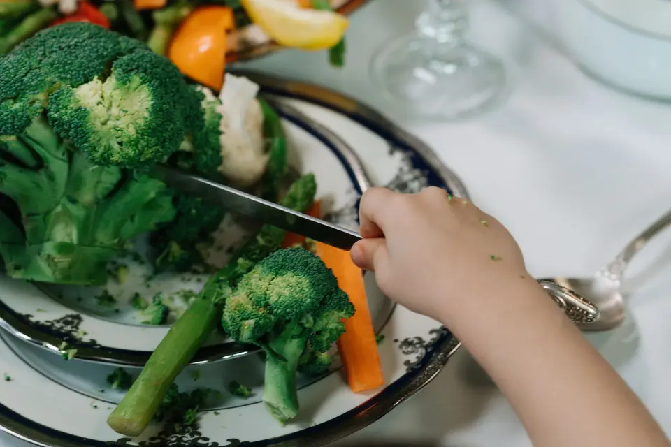 幼兒餐盤放著花椰菜與其他蔬菜，旁邊有手部準備食物