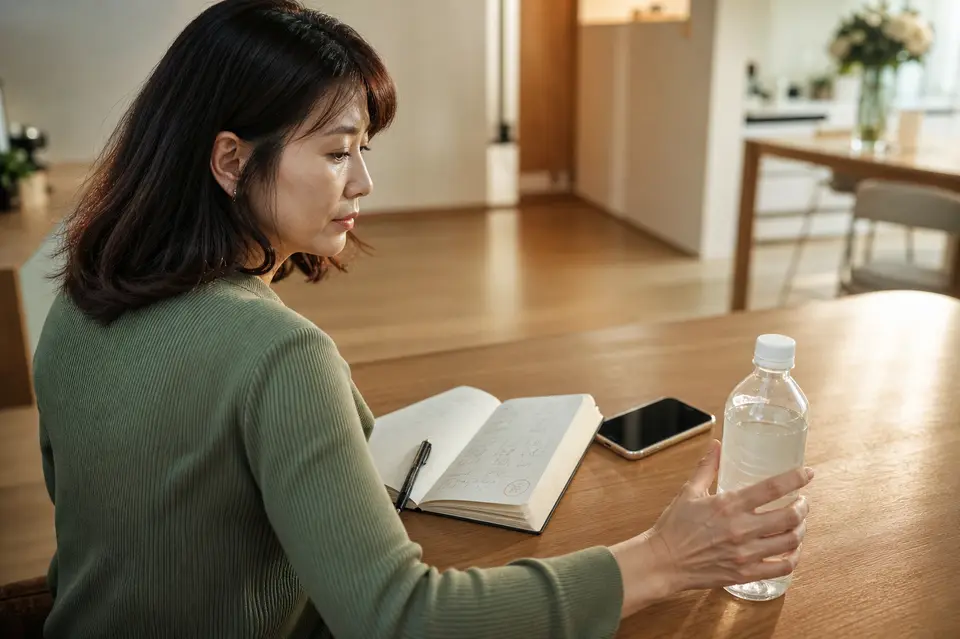 透明口服電解質液、手機與記錄症狀的筆記本放在桌上，提醒讀者辨認水瀉就醫警訊（示意圖）
